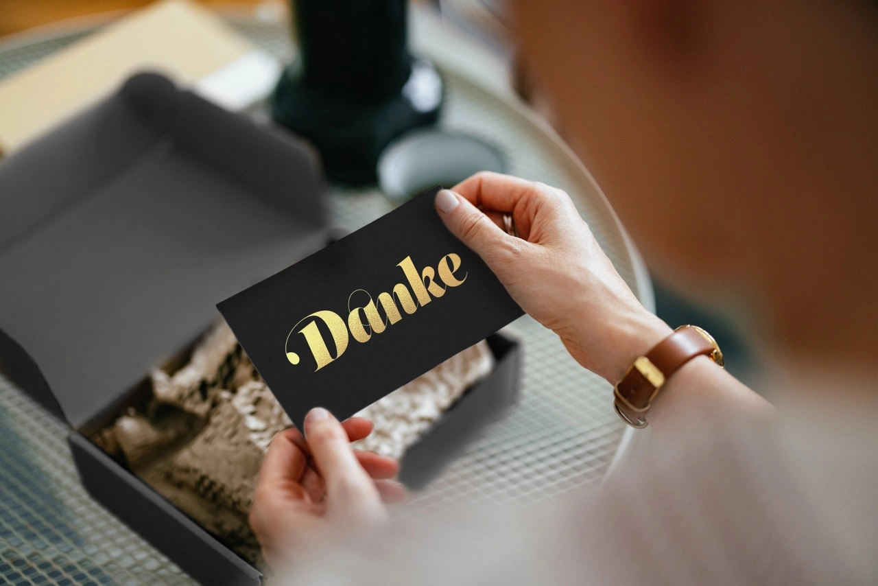 eine frau holt eine schwarze karte mit einem goldenen schriftzug "danke" aus einer Geschenkbox